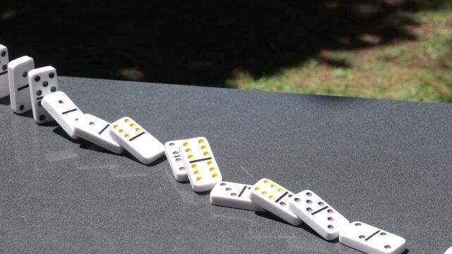 Slow motion dominoes falling in a line outdoors on a sunny day