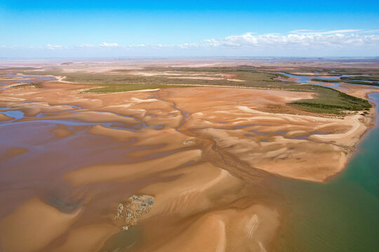 Aerial view of the winding Nullagine River through a vast arid landscape with rugged terrain and beautiful sky, Cossack, Australia.