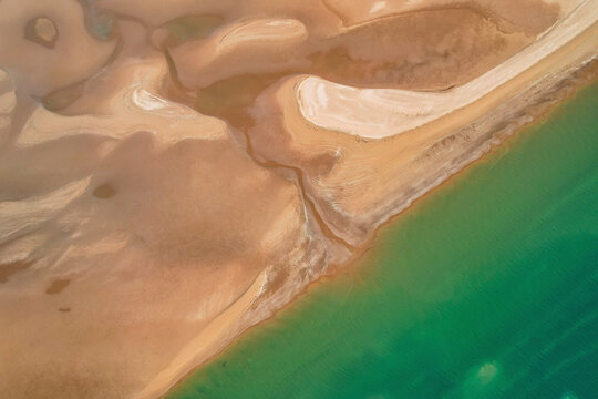 Aerial view of the serene Nullagine River winding through the vast Pilbara Region with beautiful turquoise waters and a coastal shoreline, Cossack, Australia.