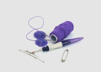 N&auml;hzubeh&ouml;r in Lila: Garnspule, Kn&ouml;pfe, Sicherheitsnadel, Nadeln und ein Nadeleinf&auml;dler. Ideal f&uuml;r kreative DIY-Projekte, Handarbeit und N&auml;harbeiten auf wei&szlig;em Hintergrund