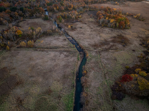 Aerial view of tranquil autumn foliage over a picturesque valley with a serene creek and forest, Dedham, Massachusetts, United States.
