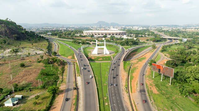 Aerial view of bustling city gate and highway with cars and greenery, Kukwaba District, Abuja, Nigeria.