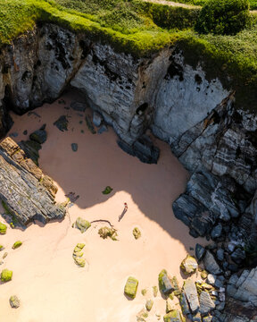 Aerial view of scenic beach with rocky cliffs and serene ocean, Tapia de Casariego, Spain.