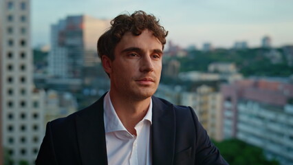 Elegant suit man standing on rooftop overlooking city at twilight closeup. 