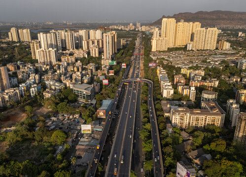 Aerial view of bustling traffic on a flyover amidst modern skyscrapers and urban landscape, Thane, India.