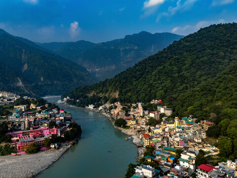 Aerial view of the serene Ganga River surrounded by vibrant mountains and the Laxman Bridge in the picturesque town of Rishikesh, Uttarakhand, India.