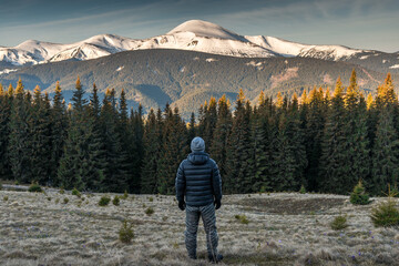 Obraz premium Rear view of young man in warm clothing embarks on a hiking trip at sunrise, surrounded by the breathtaking backdrop of snowy mountains