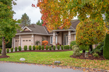 Two story stucco luxury house with garage door, big tree and nice Fall foliage landscape in Vancouver, Canada, North America. Day time on November 2024.