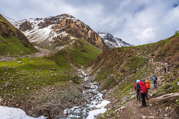 Trekkers with backpack traversing Rupin pass trail, It is full of diversity from majestic Himalayan ranges to waterfalls, glacial meadows, snow-covered landscape, lush forests.