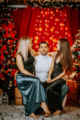 A father sits between his daughter and wife in a festive Christmas setting, with glowing lights, decorated trees, and joyful expressions.