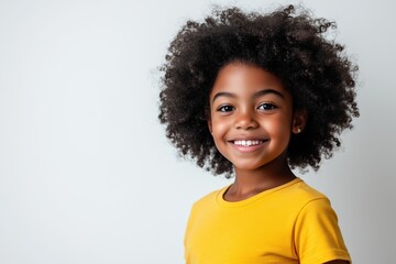 A young girl with curly hair is smiling and wearing a yellow shirt
