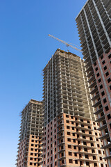 Obraz premium Three modern high-rise panel houses under construction and a tower crane against the blue sky, vertical photo.