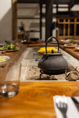 A beautifully set traditional Japanese irori hearth featuring a rustic cast iron kettle, surrounded by a warm dining setup. 