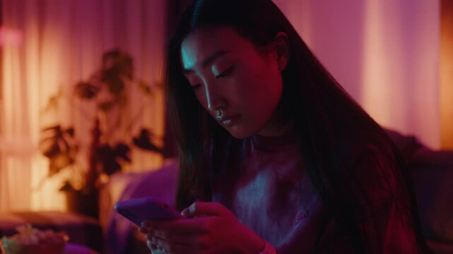 Asian Woman on Sofa in Living Room Engaged in Interaction with Her Phone in colourfull neon light 
