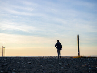 A man in headphones walks along the shore to the sea. A man goes to watch the sunset. A resort place. Solitude.