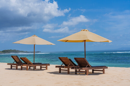 View of tranquil Nusa Dua beach with sun loungers and umbrellas under a clear blue sky, Bali island, Indonesia.