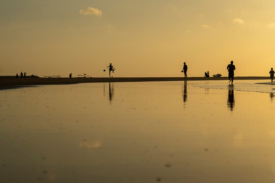 View of people playing football at Kuta Beach during sunset with serene reflections, Denpasar, Indonesia.