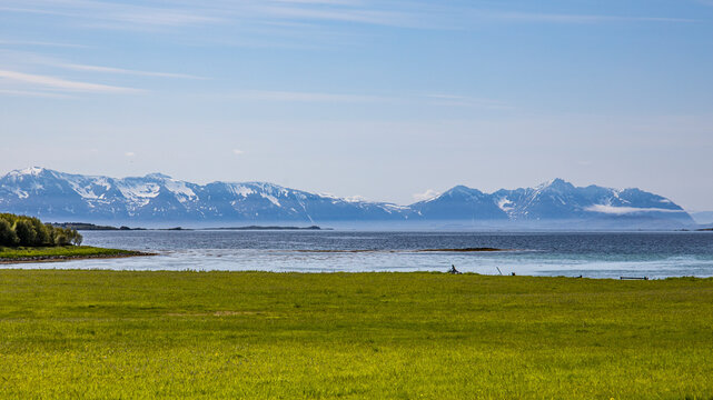 View of serene coastal meadows and majestic mountains with a picturesque village, Skrolsvik, Norway.