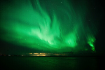 View of northern lights illuminating the night sky with vibrant green lights and stars, Reykjavik, Iceland.