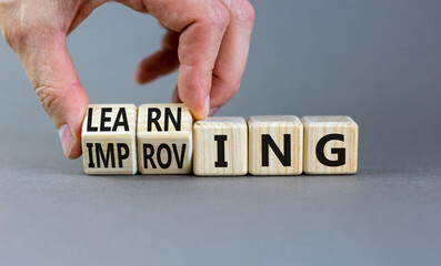 Improving or learning symbol. Businessman turns wooden cubes and changes the word Improving to Learning . Beautiful grey background. Educational business improving or learning concept. Copy space.