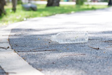 Littering plastic bottle with drinking water on the road at the green park for an environmental cleaning concept 