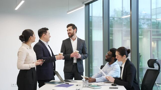 Colleagues communicate have a friendly chat during a coffee break. Group employees team business people coworkers having fun discussing project standing in office laugh indoor familiar cheerful joyful