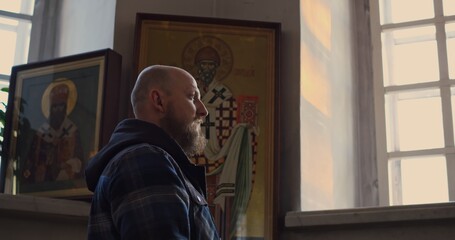Obraz premium Man praying near golden altar inside orthodox church. Peaceful moment of faith and reflection, surrounded by icons and lit candles, symbolizing spirituality and devotion. Man crossing himself