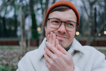 Worried man with a toothache in a park, feeling pain and stress, highlighting the importance of...