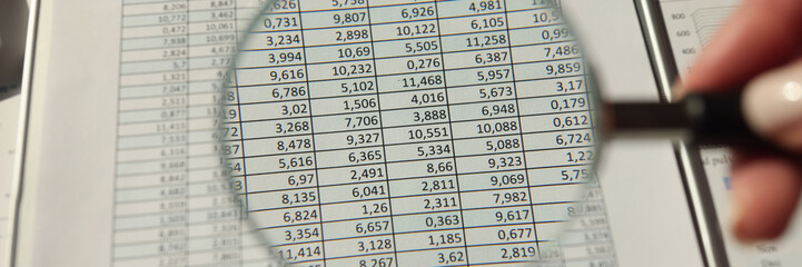 Hand of woman holds magnifier glass over accounting document