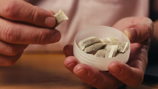 Snus nicotine tobacco close up, pack of tobacco for gum. unhealthy addiction. Man opening box with snus and taking one. 