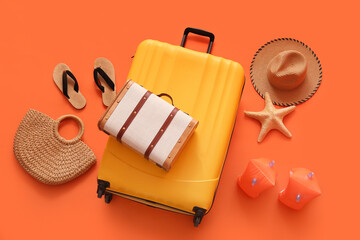 Suitcases with starfish, straw bag and beach accessories on orange background
