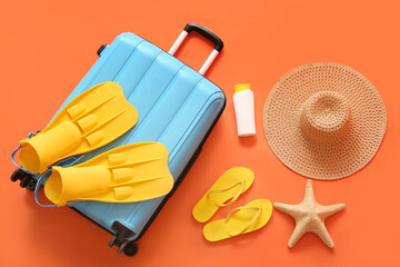 Suitcase with flippers and beach accessories on orange background