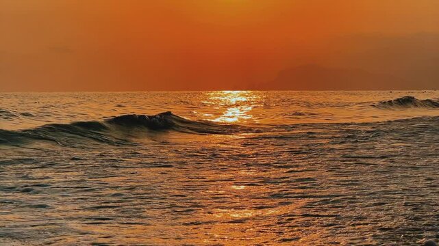 Sunset in Turkey, Alanya. The waves of the Mediterranean Sea roll over the sandy beach. The sunset is reflected in the water and slightly illuminates the city, against the background of Castle Hill.4К