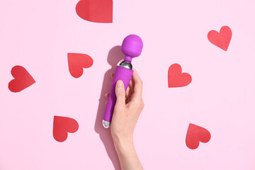 Female hand holding clitoral sex toy on pink background