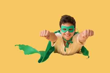 Teenage boy dressed as superhero flying on yellow background