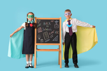 Happy pupils dressed as superheroes and blackboard with text BACK TO SCHOOL on blue background