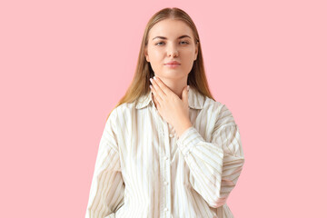 Young woman self-examining thyroid gland on pink background