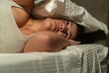 Young woman suffering from insomnia covering her head with pillow