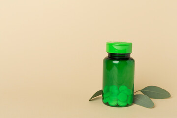 Bottles with pills and green leaves on color background