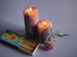 Vor zwei brennenden Kerzen liegt eine geöffnete Streichholzschachtel, daneben liegt eine...
