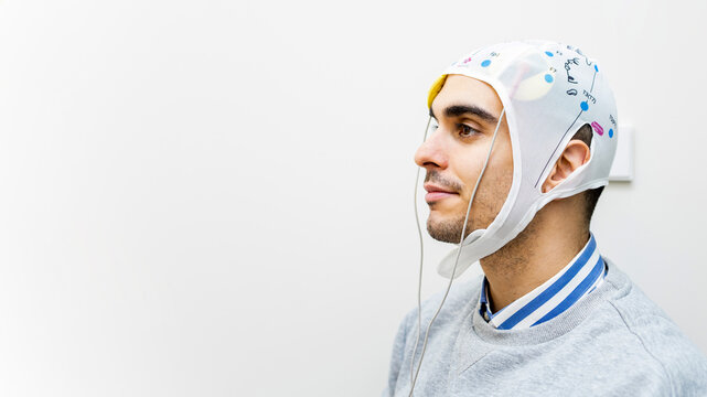 A young man undergoes transcranial direct current stimulation therapy for depressive disorders. The man is on a gray background. Copyspace for advertising.