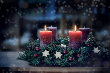 Advent wreath with the second lit candle and Christmas decoration outdoors in a patio at night in...