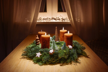 Third advent with orange brown candles on a wreath from green fir branches with Christmas...