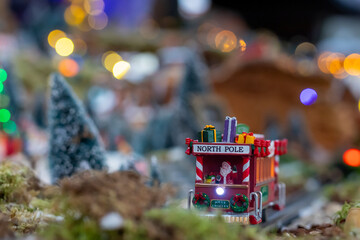 A festive miniature train labeled "North Pole" with Santa and gifts moves through a snowy village scene surrounded by trees, creating a joyful holiday atmosphere.