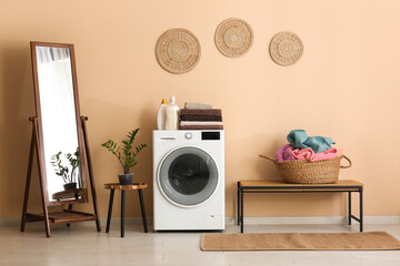 Modern washing machine, mirror, houseplant and basket with laundry in room