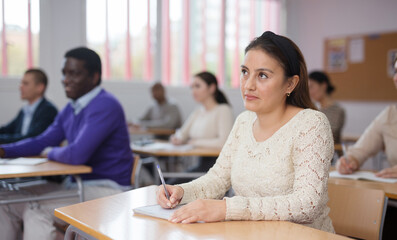 Focused young attractive Latina listening to lecture in classroom with group. Postgraduate...