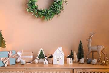 House shaped candle holders with Christmas trees and balls on commode near beige wall in room