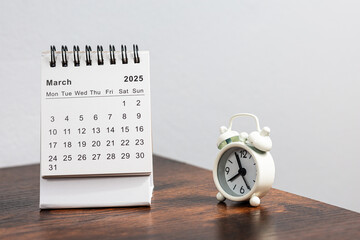 March 2025 calendar and alarm clock on a wooden desk - month page