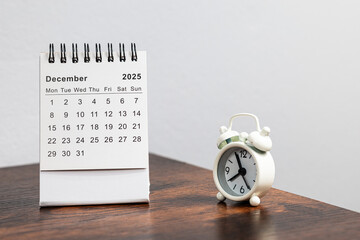 December 2025 calendar and alarm clock on a wooden desk - month page