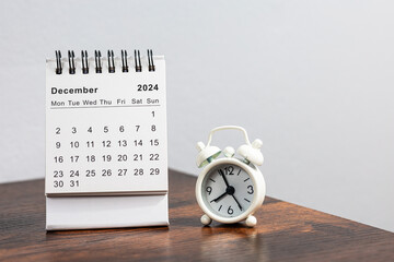 December 2024 calendar and alarm clock on a wooden desk - month page